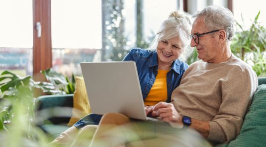 Senior couple using laptop while sitting on sofa in living room at home